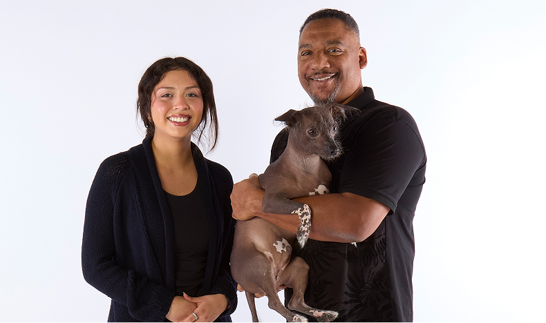 Two people pose together, one holding a dog in his arms.