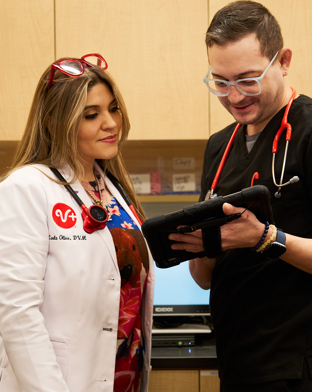 A vet tech shows a veterinarian something on a tablet.