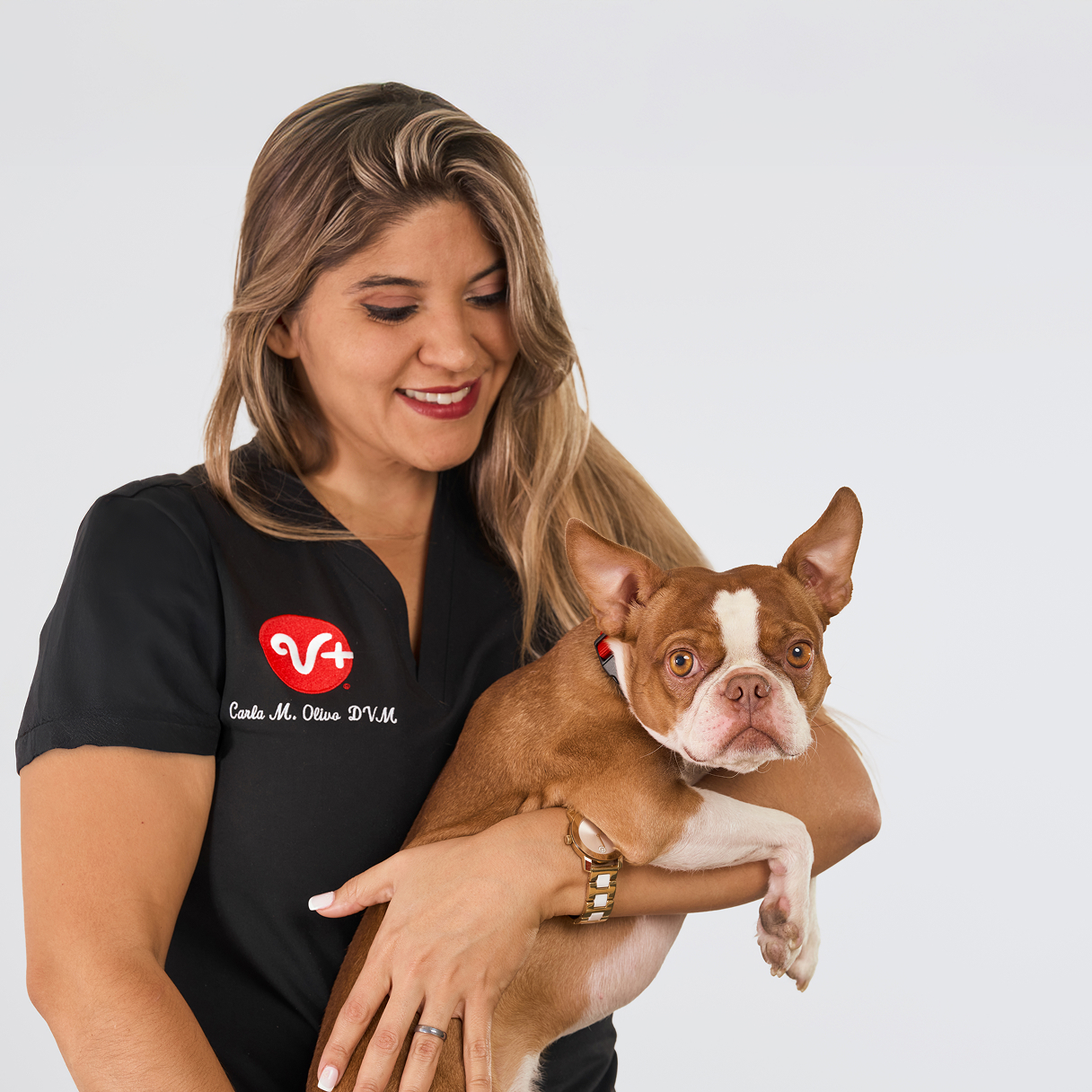 A veterinarian smiling at a small dog in her arms.