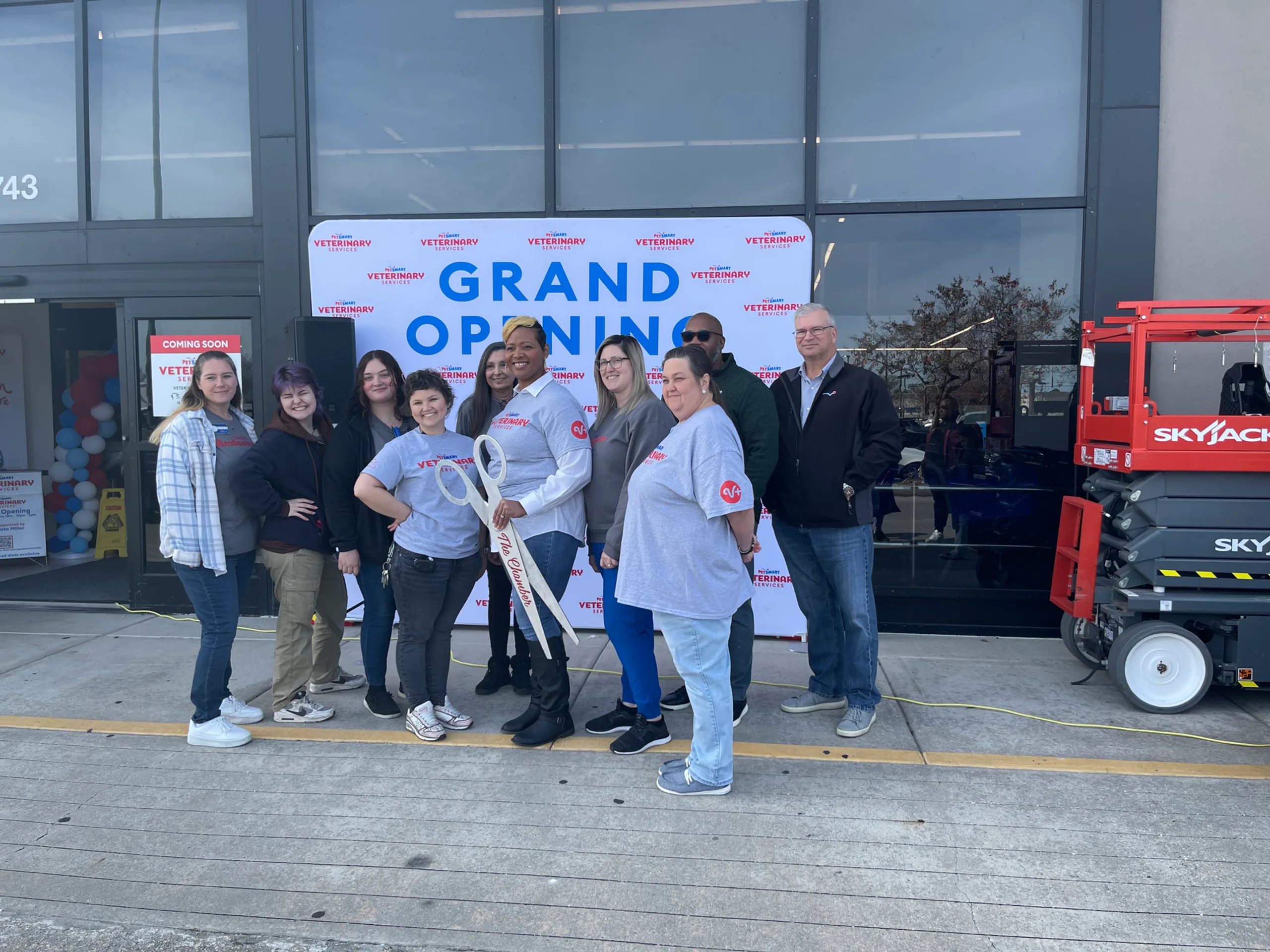 Holding big scissors in front of grand opening sign